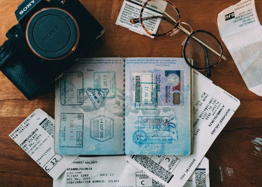 A desk with travel items on it: a passport, a camera, stamps, and a pair of glasses. 