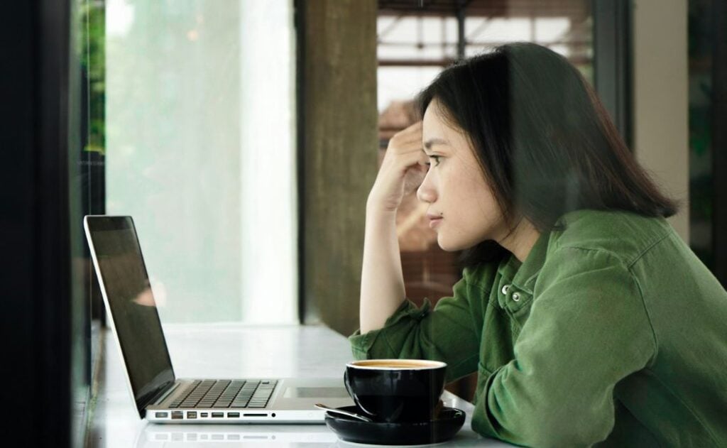 A woman in a green sweater working on a laptop with a cup of coffee.