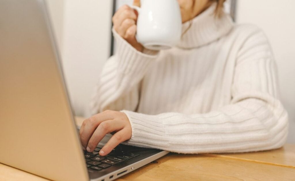 A woman sipping coffee while working on a computer.