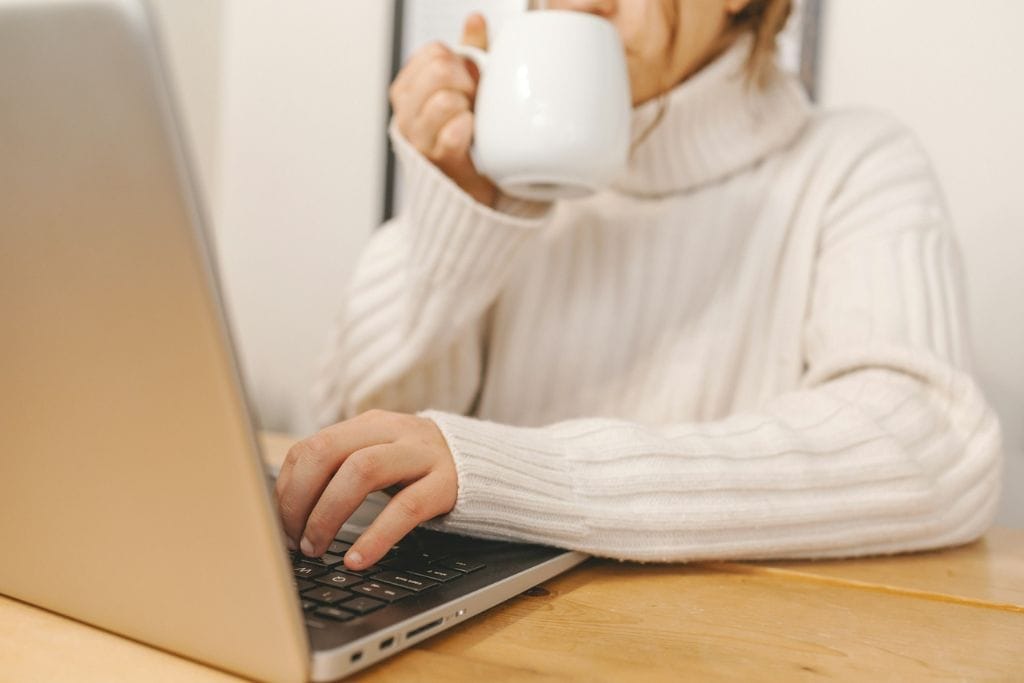 A woman sipping a cup of something while she works at her laptop. 